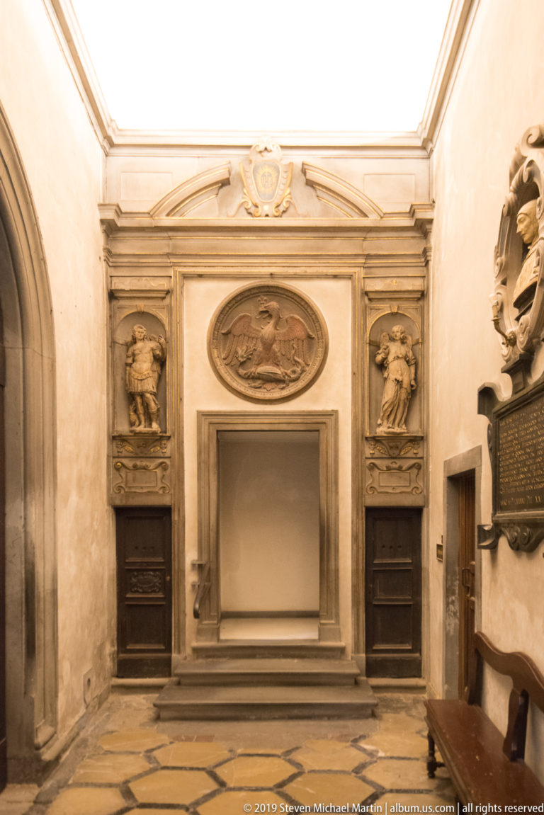 Stone wall monument with central recess, oval relief, pilasters, carved side panels, and dark inscription plaques.