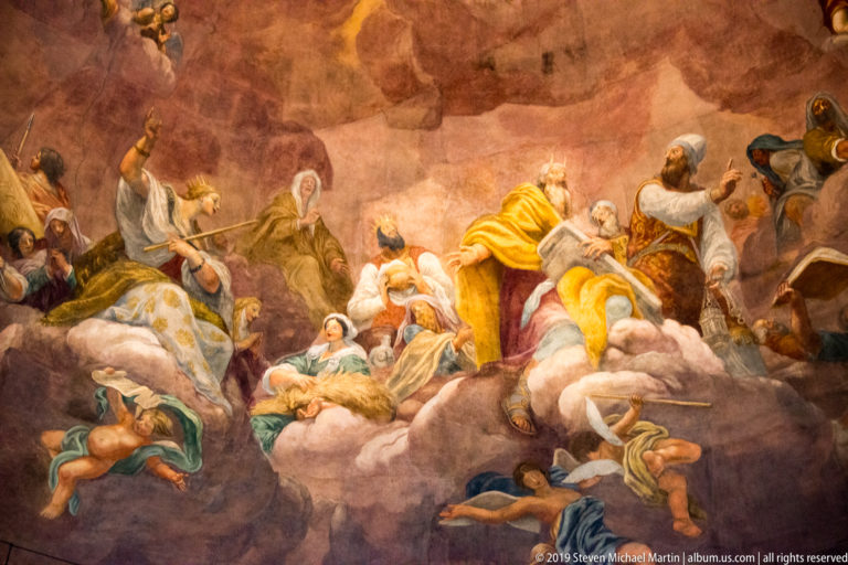 Detail of a dome fresco showing sacred figures and angels gathered on clouds in warm-colored robes.