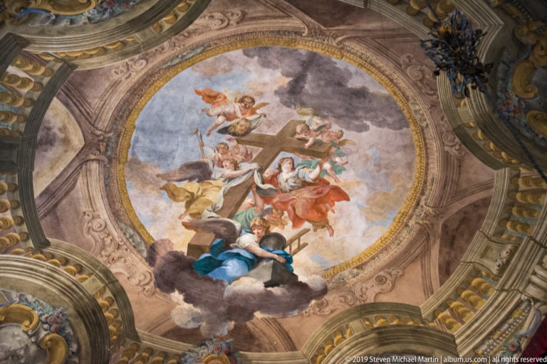 Circular ceiling fresco with sacred figures and angels among clouds, framed by painted and gilded architecture.