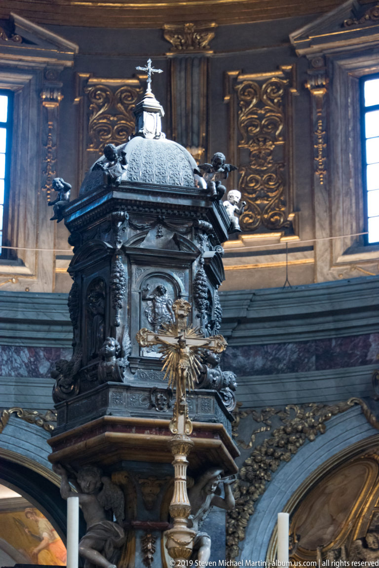Dark domed church furnishing with relief panels and gilded details inside the ornate basilica.