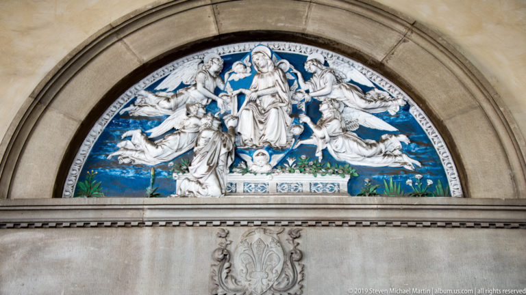 Blue-and-white glazed terracotta lunette of the Madonna and Child surrounded by angels.
