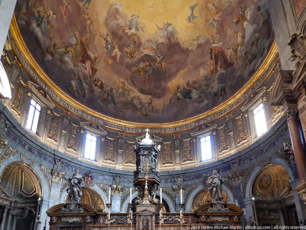 Frescoed dome and windowed drum above monumental altar furnishings and sculptural structures in the sanctuary.