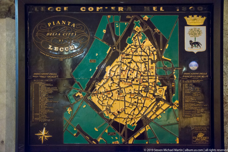 Decorative map of Lecce showing the dense historic street plan within a dark perimeter, with legends, compass rose, and civic crest.