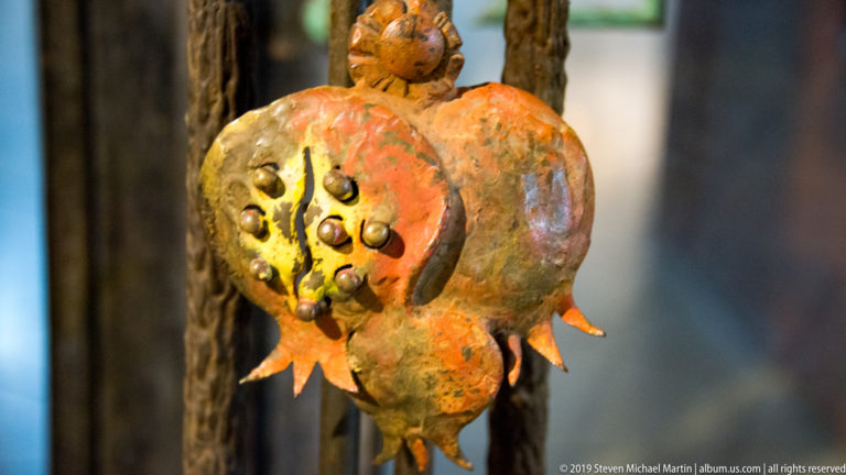 Orange-red pomegranate-shaped hanging ornament with clustered seed-like bumps and pointed sepals against a dark background.