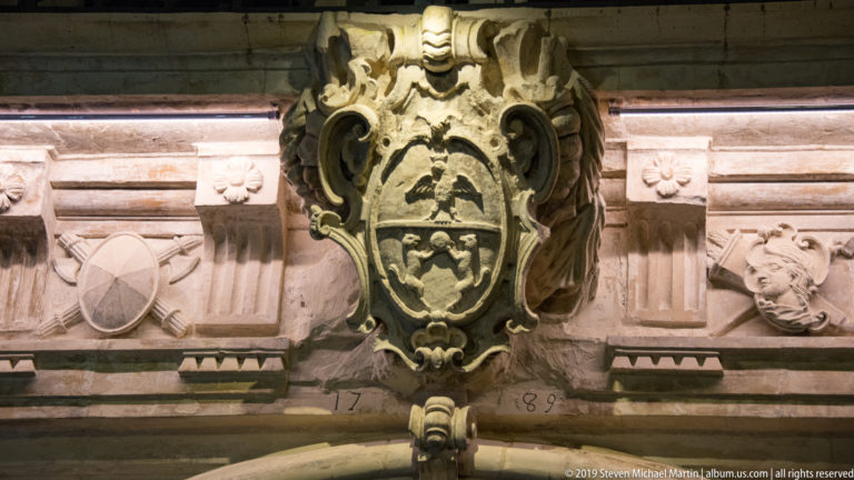 Large carved heraldic cartouche above an arch, flanked by relief panels and the divided date 17 and 80.