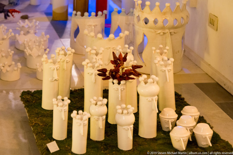 Cluster of white ceramic tower and vessel forms with rounded finials arranged on a dark moss-like base indoors.