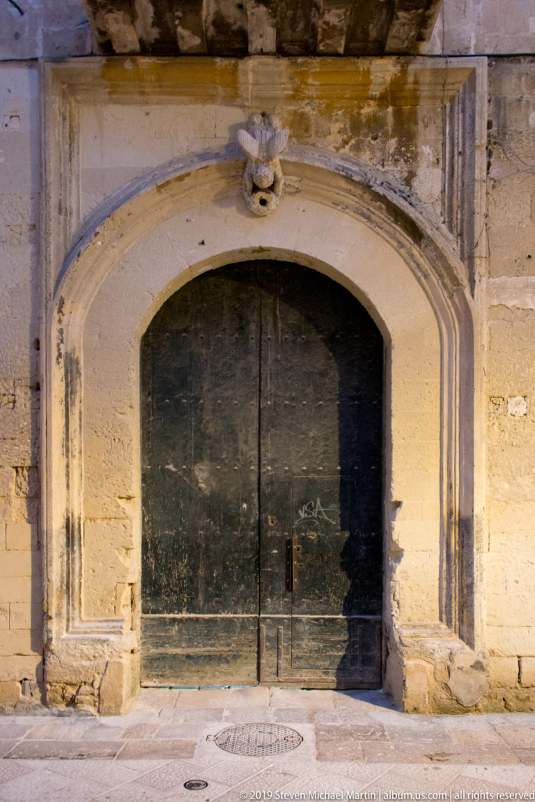 Large dark wooden double doors set in a shallow molded stone arch with a small carved ornament above.