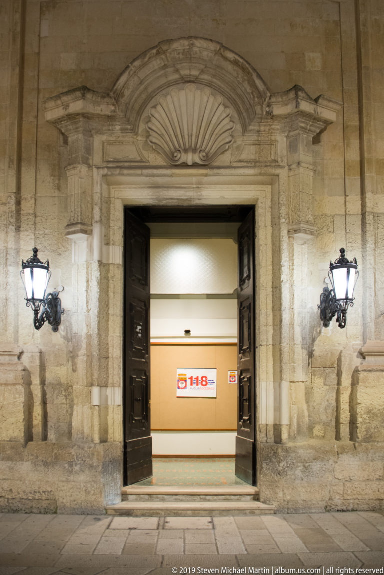 Open stone portal with dark wooden doors, wall lanterns, a shell-shaped overdoor, and a brightly lit interior marked 118.