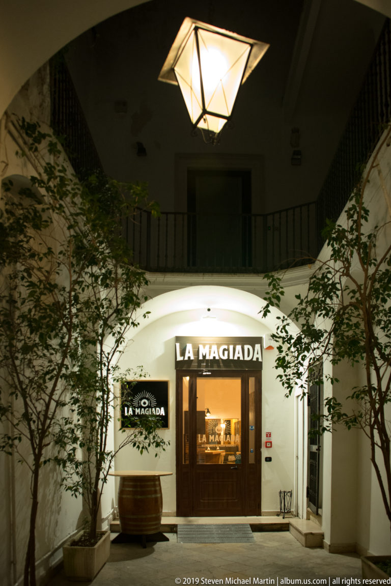 White vaulted courtyard with a large hanging lantern and illuminated entrance marked LA MAGIADA.