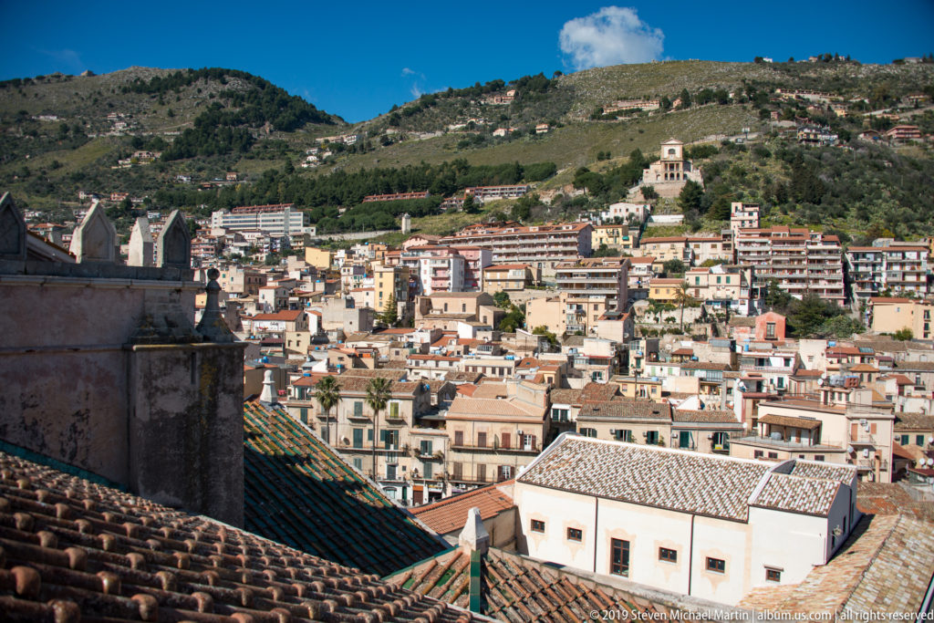 Terracotta roofs lead toward hillside houses and a small ridge-top building in Monreale.