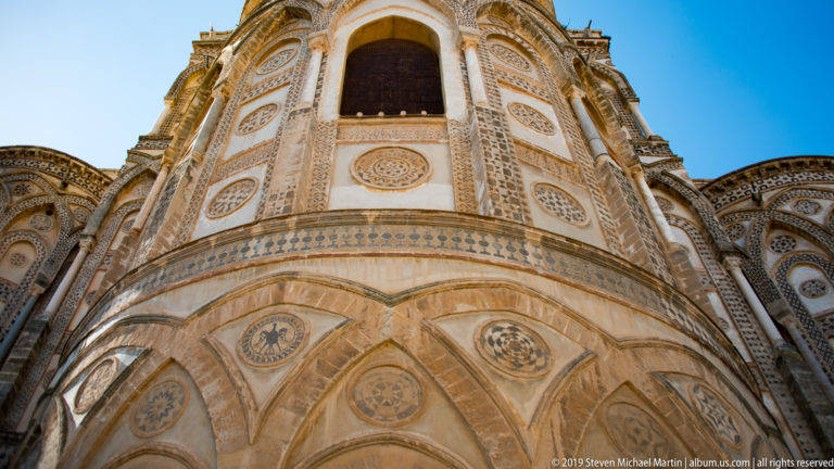 A tall arched opening and geometric stone inlay rise above a band of medallions on the cathedral façade.