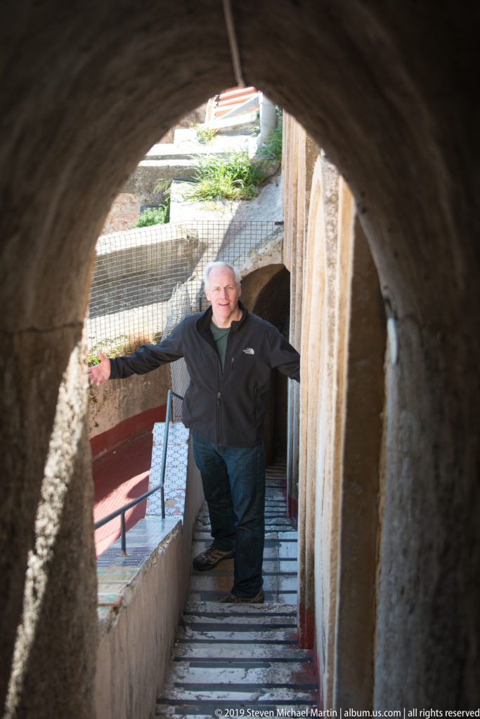A visitor stands on steps beneath a stone arch, holding the wall beside a bright landing.