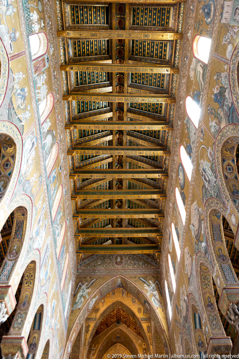 A richly patterned wooden ceiling fills the view above the nave, bordered by high windows and decorated arches.