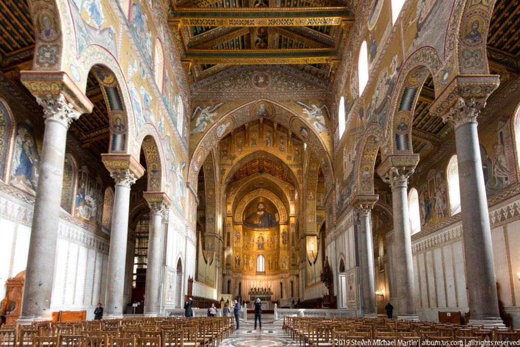 The cathedral’s long nave recedes between pale columns and arches toward a brightly illuminated, gold-decorated sanctuary.
