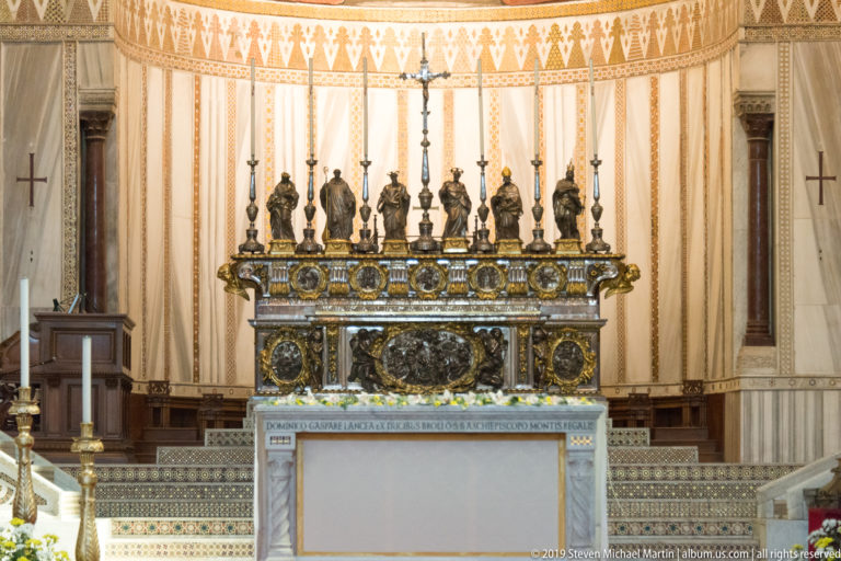 A pale altar and rows of candlesticks stand beneath an ornate carved canopy.