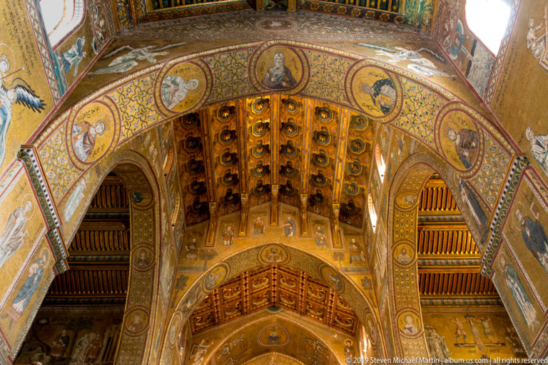 A decorated coffered ceiling meets a mosaic arch with small medallions and bright windows.