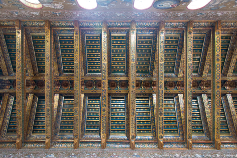 Blue and dark ceiling panels with gold ribs form a grid above a row of pale arches.