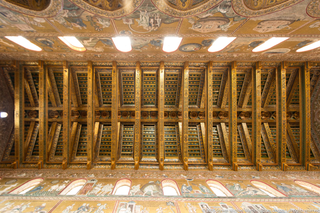 Rows of dark, gold-edged ceiling coffers extend above a long arcade of pale arches.
