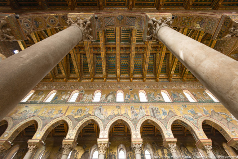 Pale columns rise toward a dark coffered ceiling decorated with gold and blue patterns.