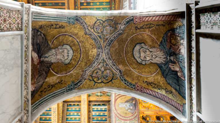 Two haloed figures face one another across a patterned gold mosaic ceiling panel.