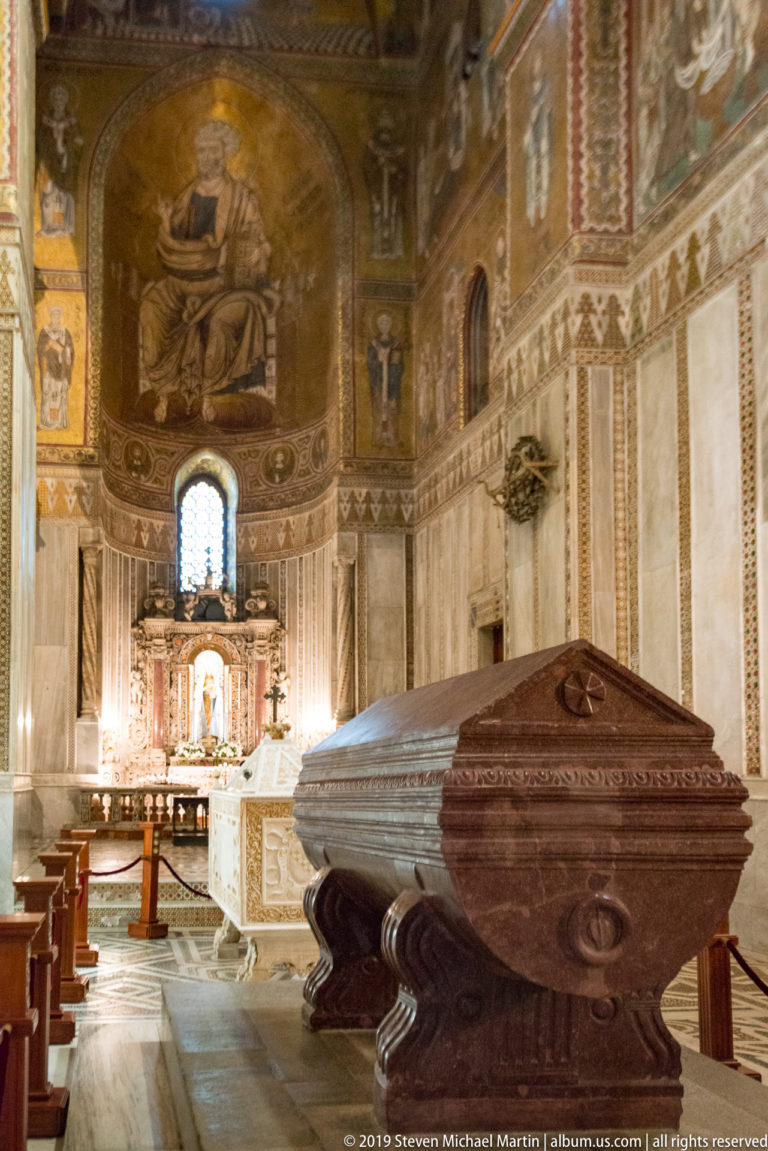 A large dark wooden lectern stands before the cathedral’s bright altar and mosaic apse.