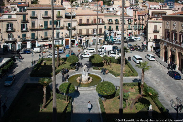 Piazza Vittorio Emanuele II seen from above, with the Triton Fountain among clipped hedges and palms.