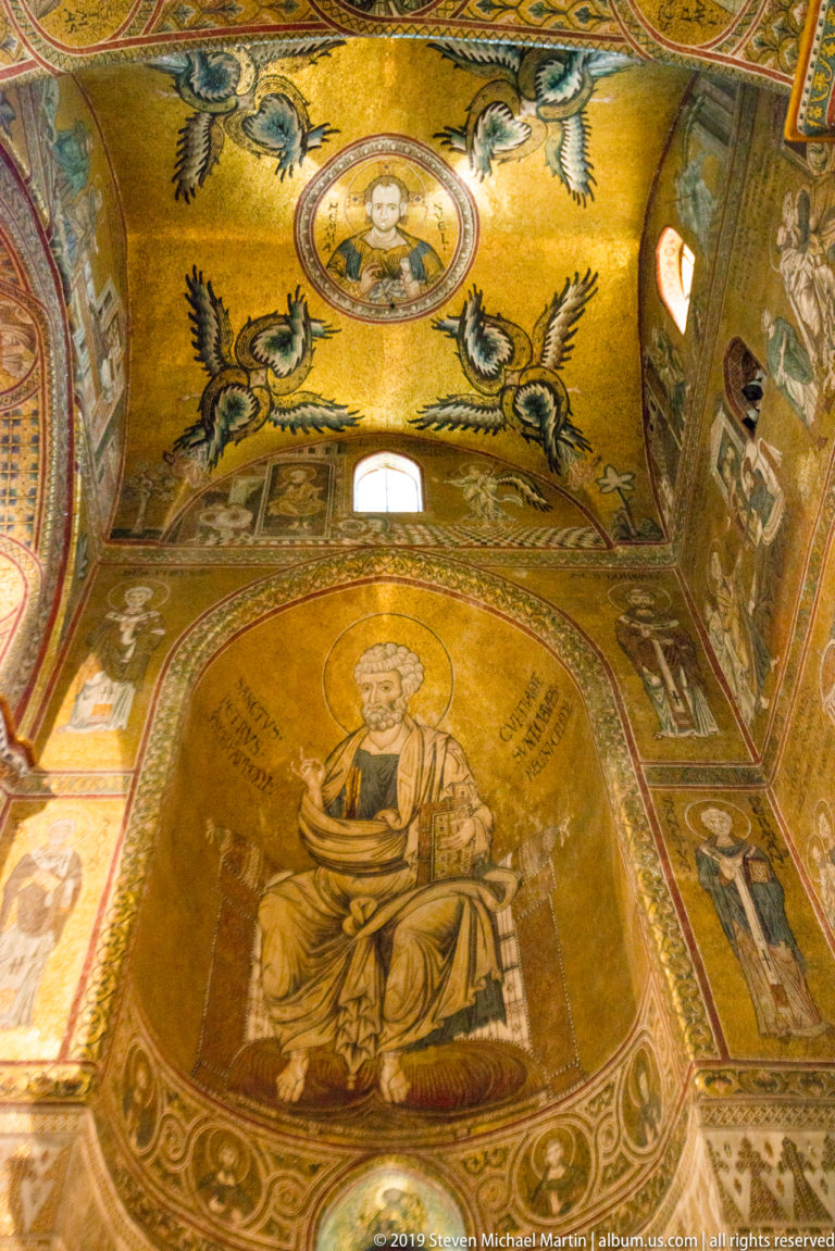 A small haloed figure and four winged creatures appear above a seated figure in gold mosaic.
