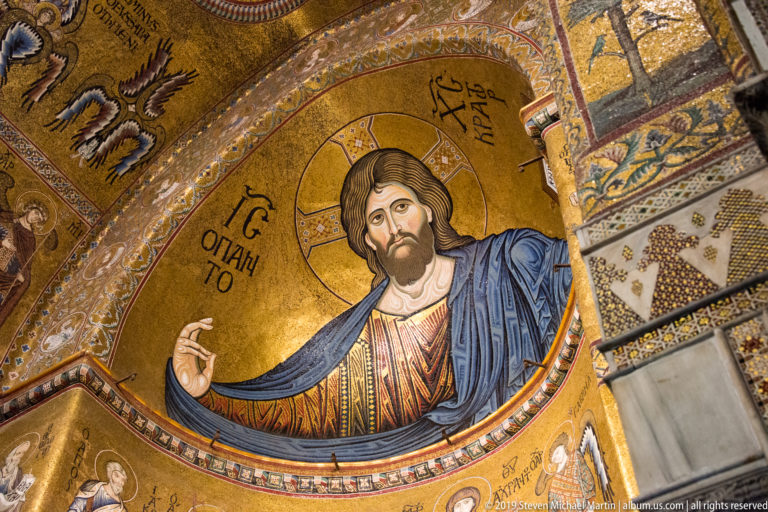A haloed Christ raises a hand and holds an open book in a gold apse mosaic.