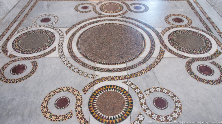 Oval and circular stone inlays form a repeating geometric pattern across a pale floor.