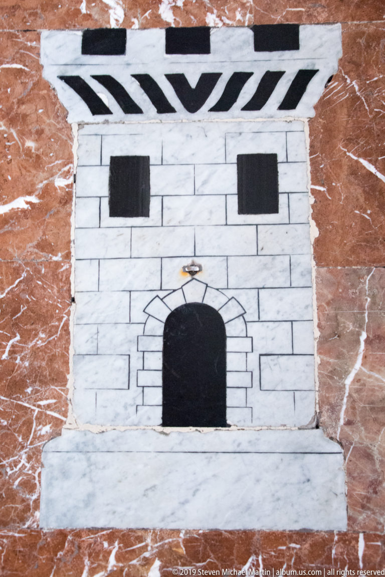 A small dark arch and stone sill are set into a pale masonry wall.