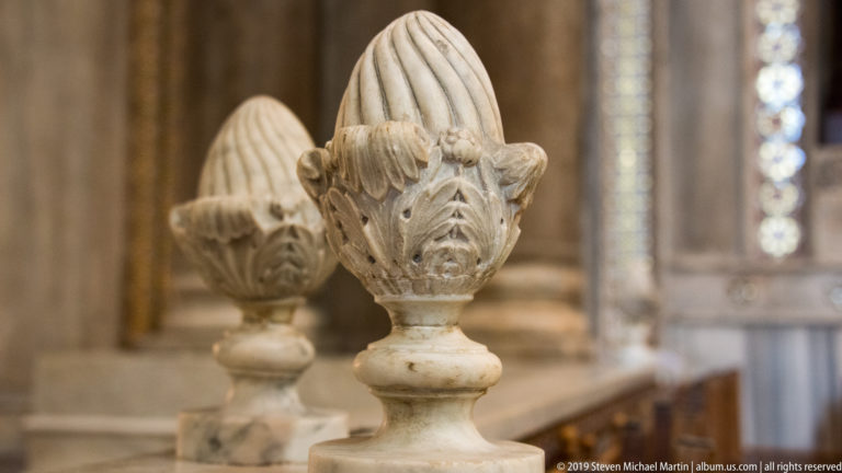 Two pale carved animal-like heads face one another in a close architectural detail.