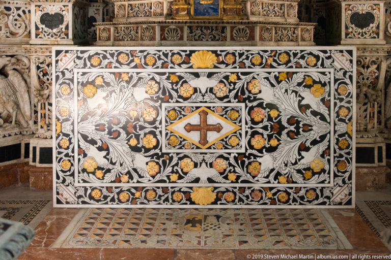 A dark cross sits in a pale diamond at the center of a floral marble inlay panel.