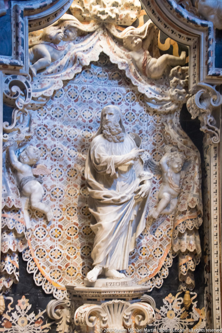 Ezekiel holds a scroll beneath an ornate arch, with a kneeling figure at his side.