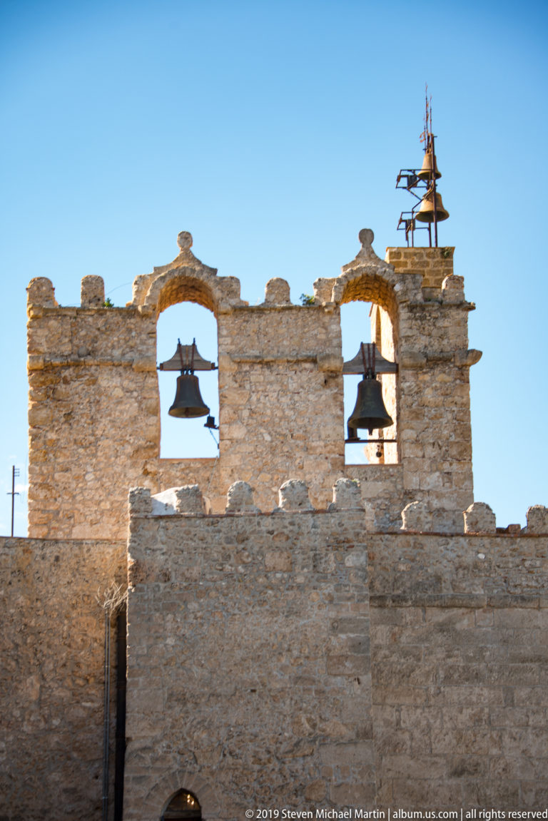 Two bells hang in arched openings high in a broad stone cathedral tower.