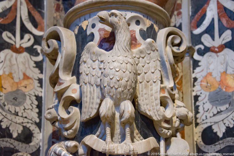 A carved eagle spreads its wings inside a circular frame surrounded by colorful inlay.