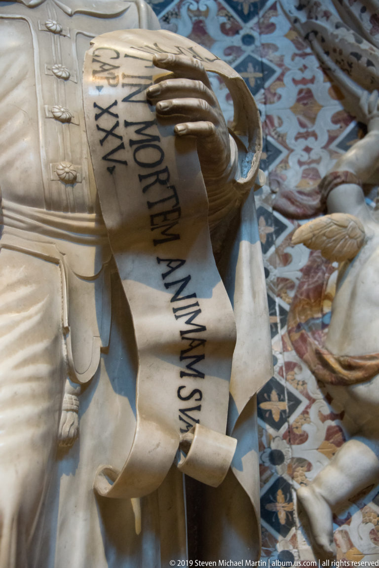 A marble prophet holds a scroll marked “ISAIAS” amid blue geometric inlay.