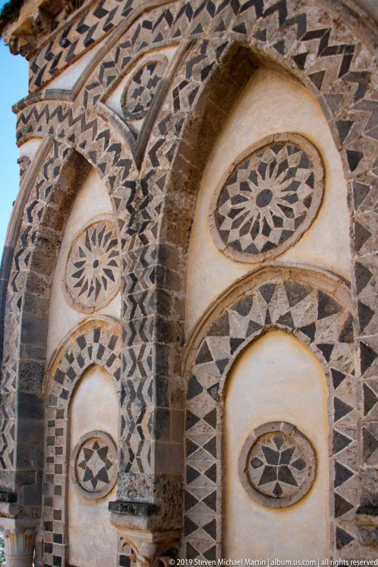 Interlocking dark and pale geometric inlay and round medallions decorate a series of cathedral arches.