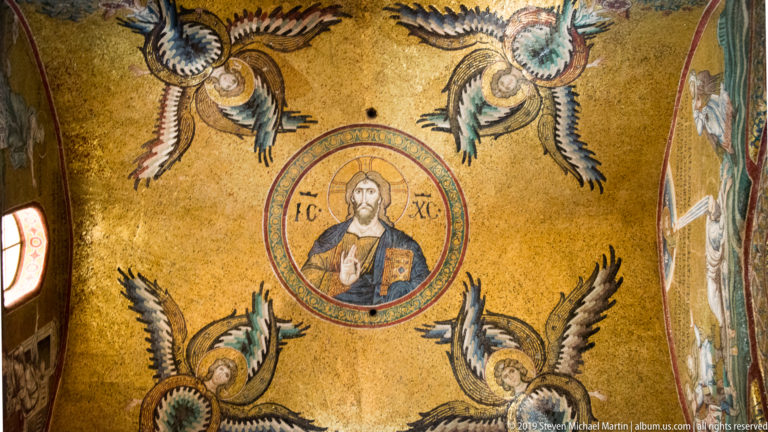 Christ raises a hand and holds a book inside a circular mosaic medallion surrounded by angels.