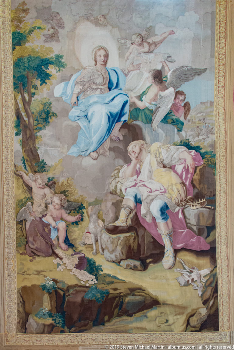 A colorful mosaic panel shows a central standing figure among seated and reclining people in a landscape.