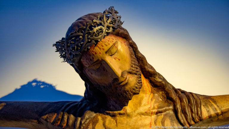 A crowned, bearded male sculpture is seen in profile against a clear blue sky.