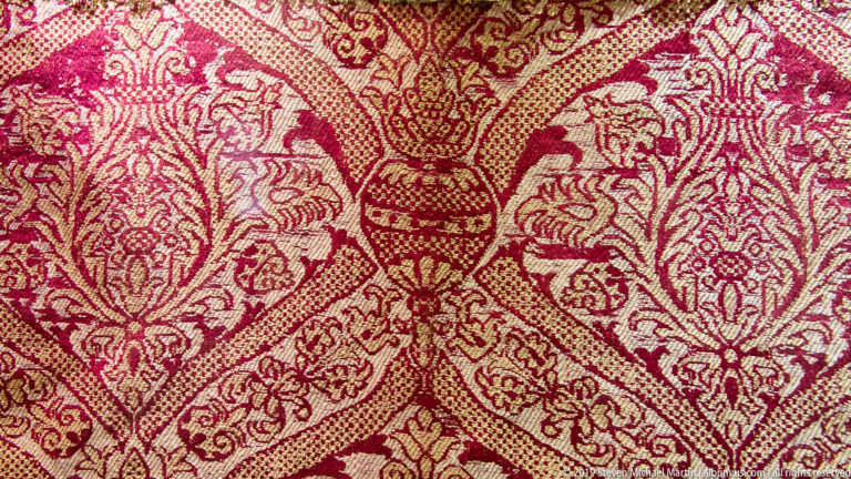 A dense red, cream, and gold mosaic forms a symmetrical pattern around a narrow central motif.