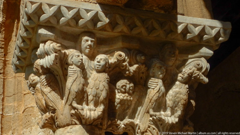A carved capital crowded with standing figures and smaller forms beneath a stone abacus.