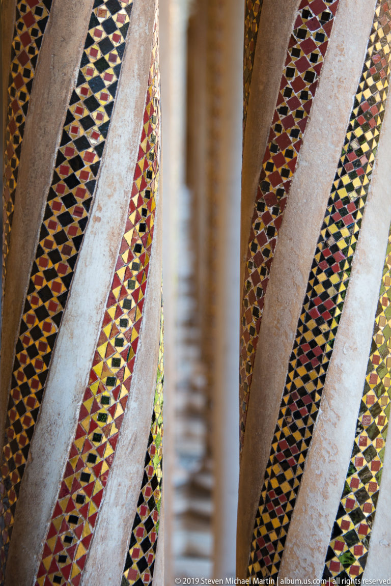 Close view of colored geometric bands decorating pale stone cloister columns.