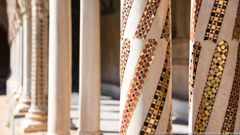 Two pale cloister columns with red, yellow, blue, and black geometric inlay.