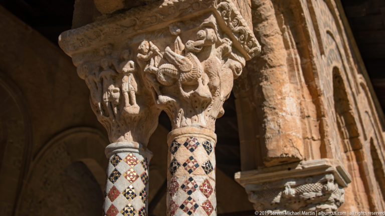 A carved capital with animal and human forms above columns decorated in colored geometric patterns.