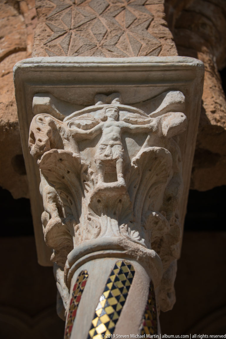 A close view beneath a carved capital, with small figures and a patterned column shaft.
