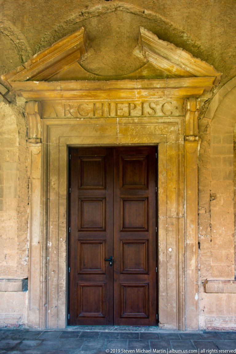 Dark double doors sit beneath a carved stone lintel and ornamented entrance hood.