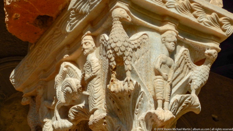 A large central carved figure rises above smaller forms on a stone capital.