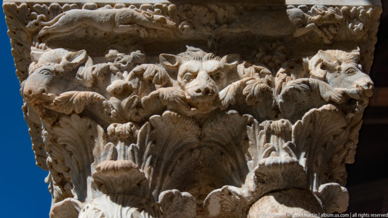 A close-up of a stone capital crowded with carved animals, foliage, and small figures.