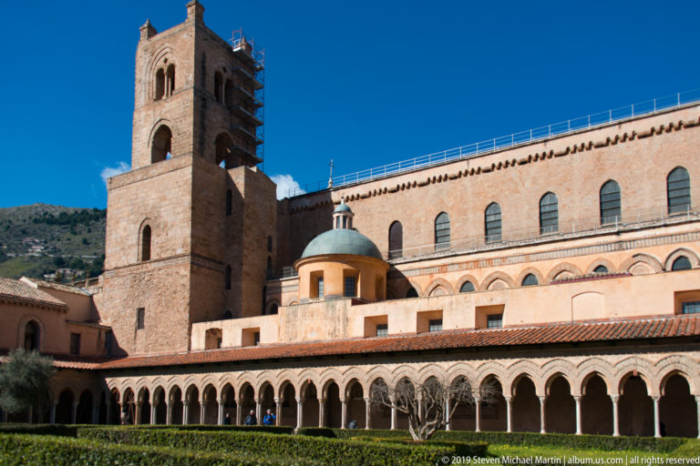 A square stone tower rises above the long arcaded wall of the cloister complex.
